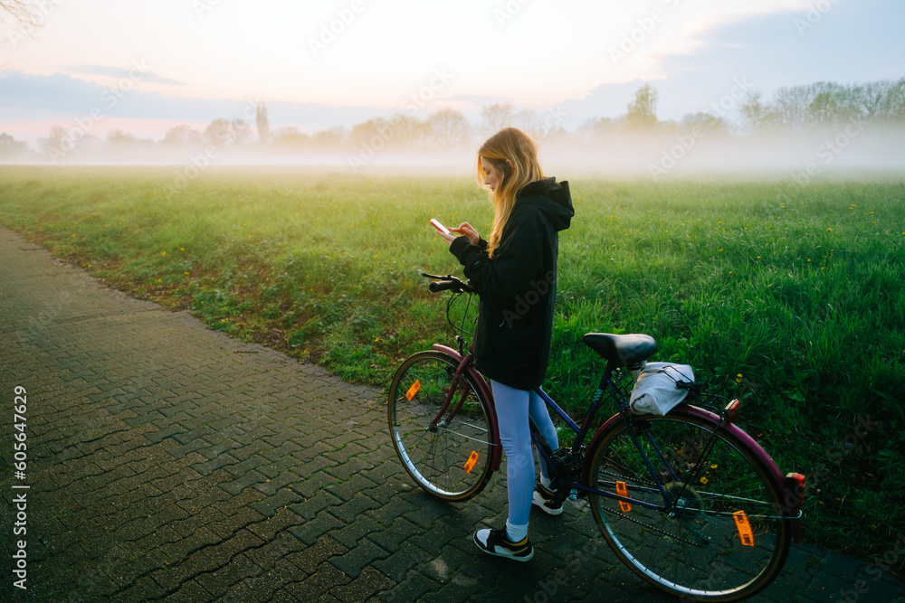 Young attractive caucasian woman using mobile phone, ride on bicycle in the park in sunset with fog . Young attractive caucasian woman using mobile phone, ride on bicycle in the park in sunset with fog .