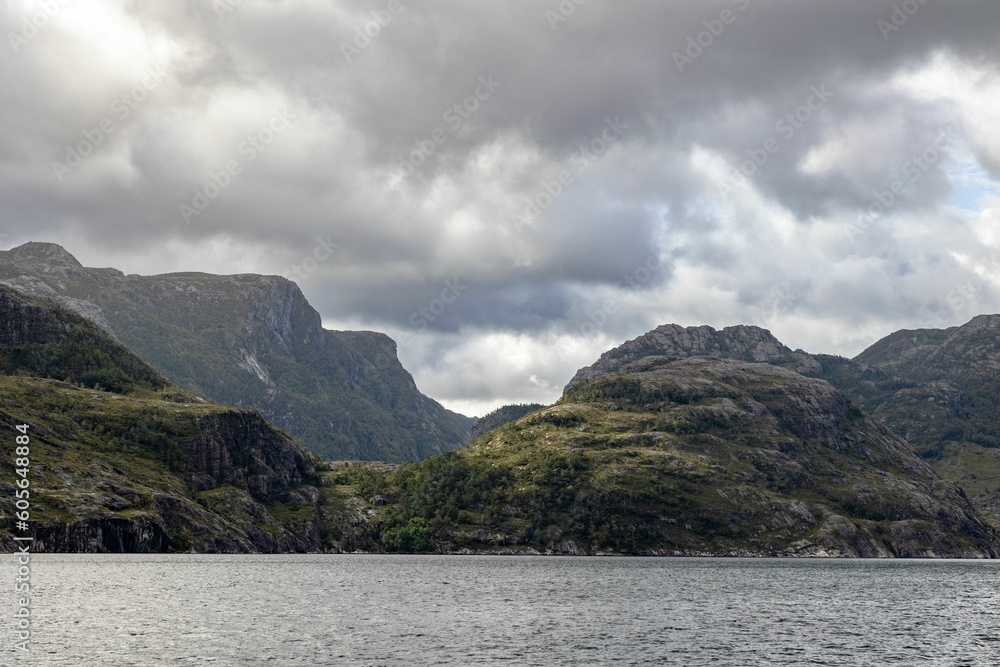 Scenic view of huge rocky mountains in cloudy sky background surrounded by the lake