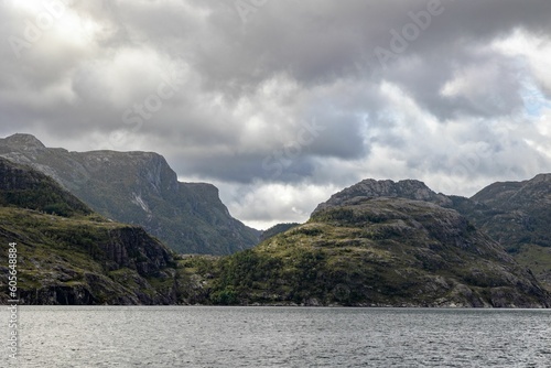 Scenic view of huge rocky mountains in cloudy sky background surrounded by the lake