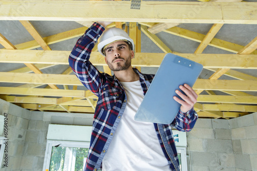 male worker holding a clipboard checking wood beams