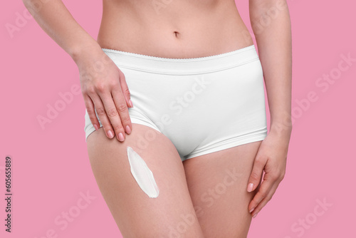 Woman with smear of body cream on her leg against pink background, closeup