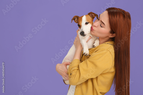 Woman kissing her cute Jack Russell Terrier dog on violet background. Space for text