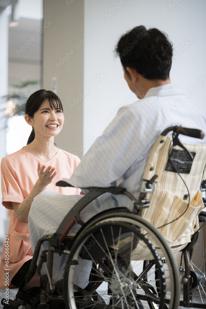 病院内での看護師と車いすに乗った患者の会話の様子 縦 病院内での看護師と車いすに乗った患者の会話の様子 縦