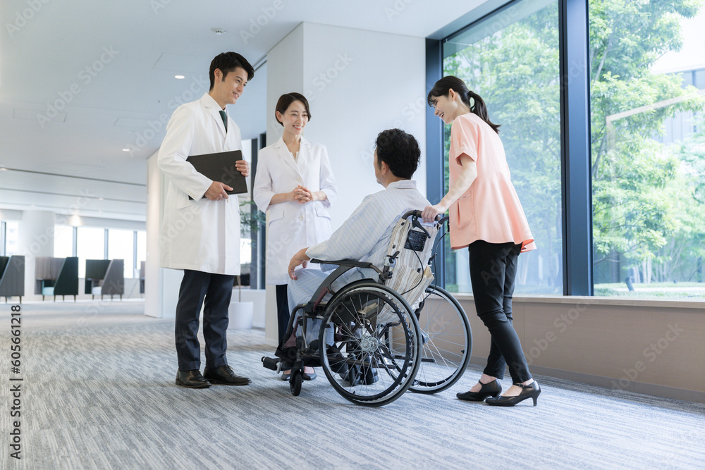 大きな病院で介護や看護される車いすに乗った男性とドクターと看護師の様子