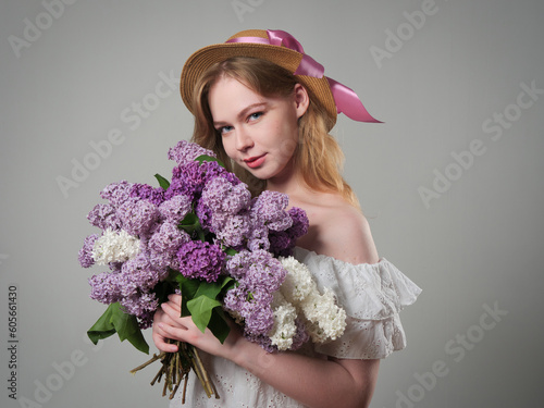 beautiful girl with blue eyes with a bouquet of lilacs on a gray background in the studio