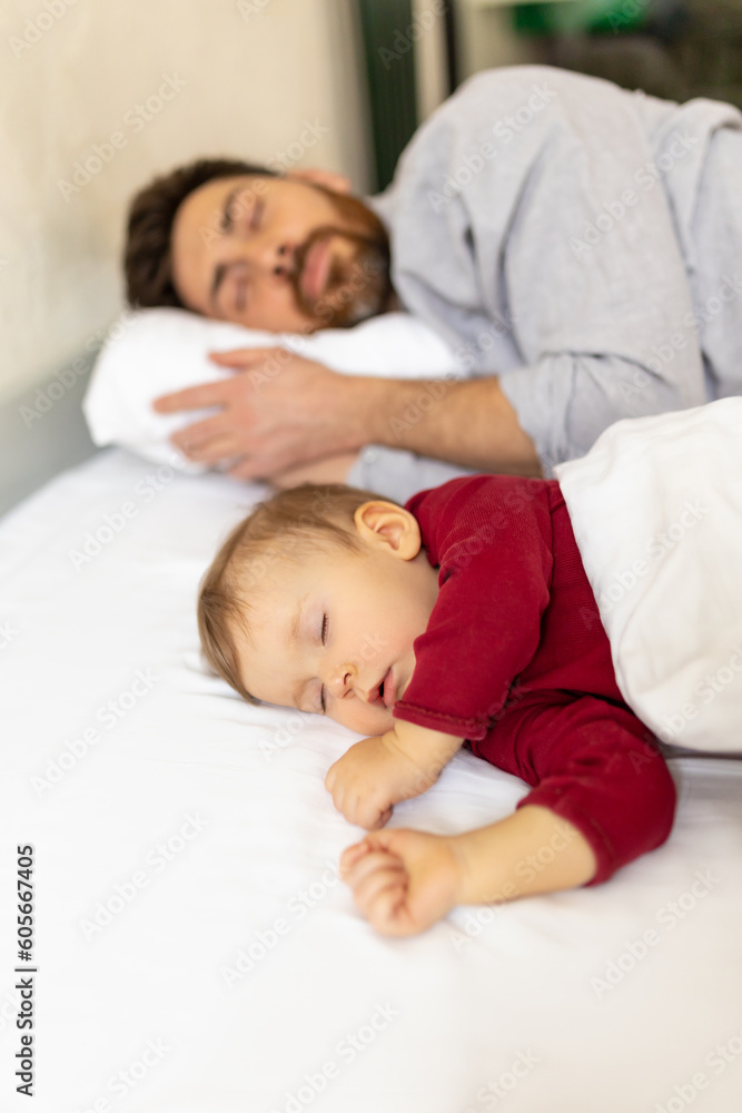 Bearded man sleeping together with infant daughter in bed.