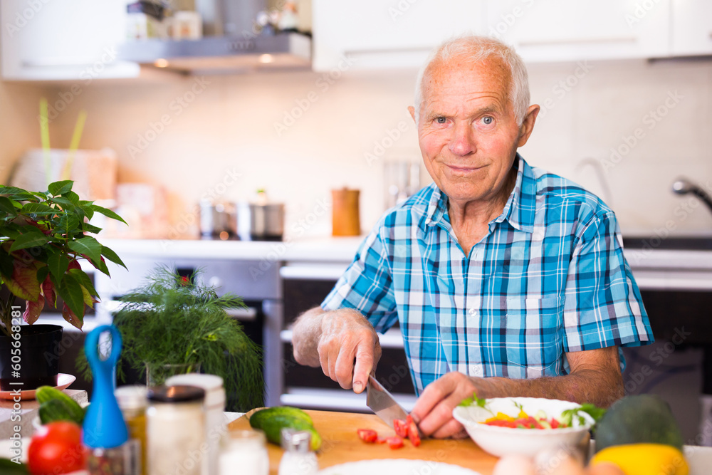 elderly man cuts vegetables for salad at the table in the kitchen elderly man cuts vegetables for salad at the table in the kitchen