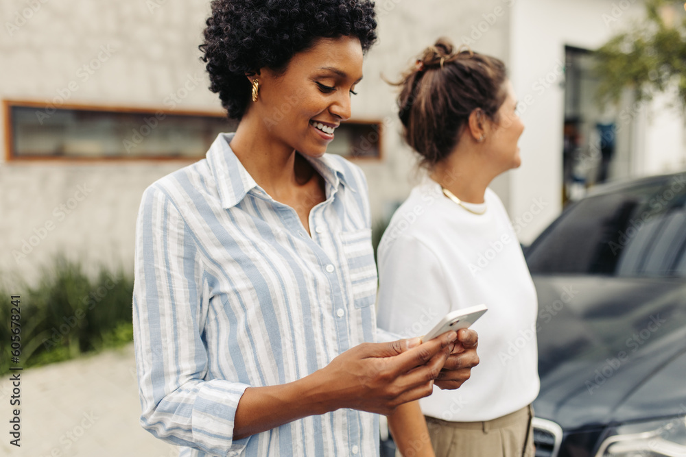 Happy young woman e-hailing a taxi while standing with her friend Happy young woman e-hailing a taxi while standing with her friend