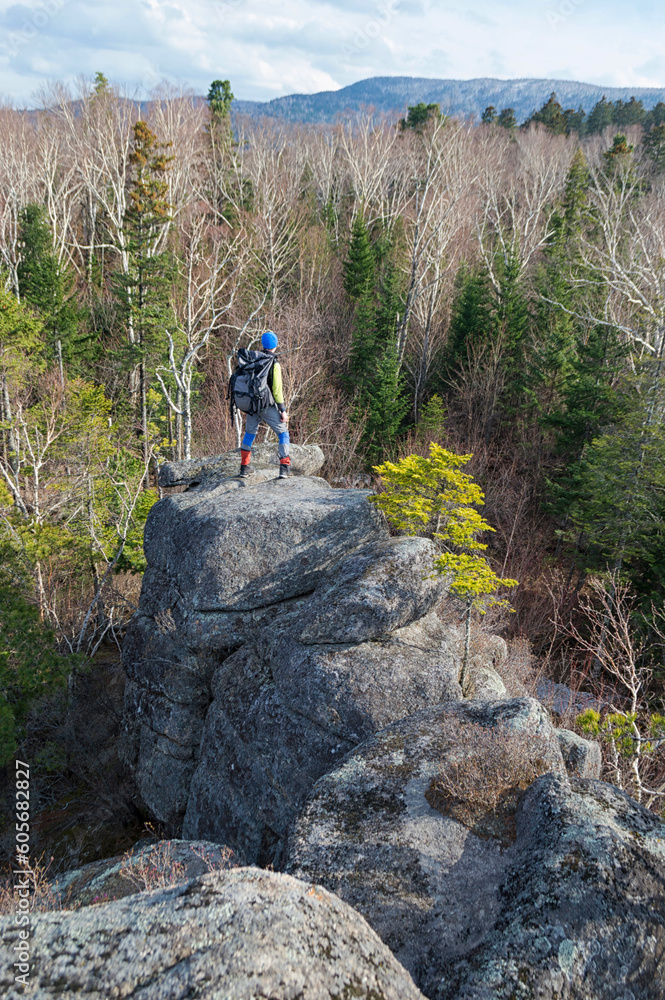 Tourist with backpack standing on the top of the rock in the spring taiga forest and enjoying virgin nature. Raven rocks. Bolshekhekhtsirsky Nature Reserve. Khabarovsk  Krai, far East, Russia.