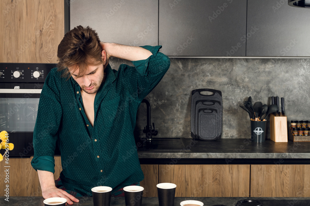 Sleepy man addicted to coffee cant stop drinking in the kitchen, many cups scattered around a table. caffeine addiction concept. - obrazy, fototapety, plakaty 