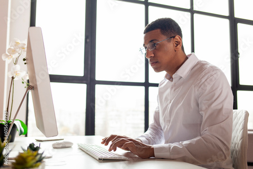 African American business man in shirt sits at table and types on computer, office worker guy works in the office