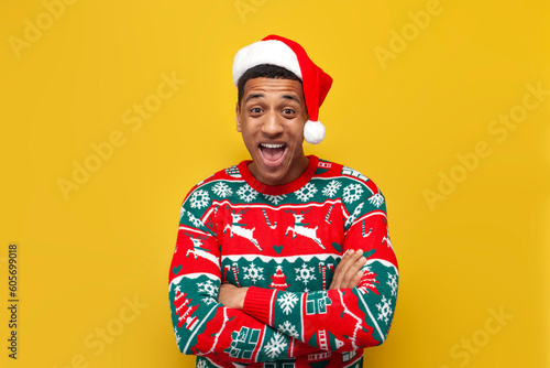 young guy in New Year's clothes and santa hat is surprised and shouts on yellow isolated background