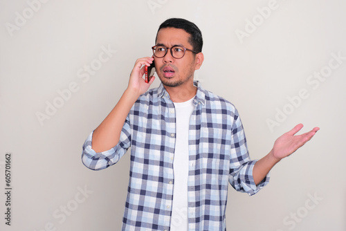 Adult Asian man showing worried expression during a phone call photo