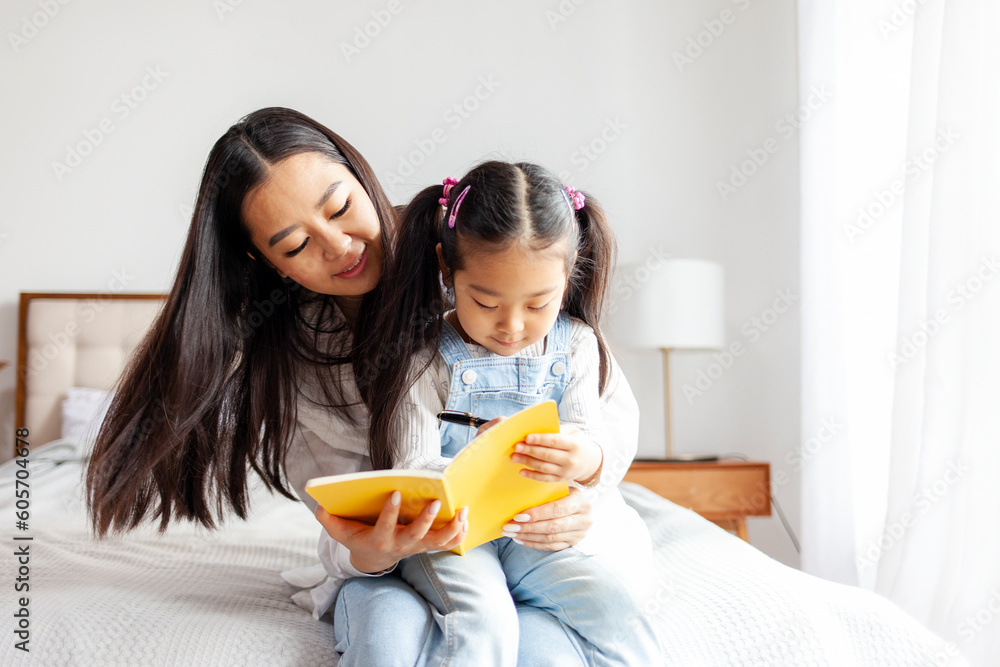 asian mother teaches daughter to read and write at home on bed, little korean girl writes in notebook with parent asian mother teaches daughter to read and write at home on bed, little korean girl writes in notebook with parent