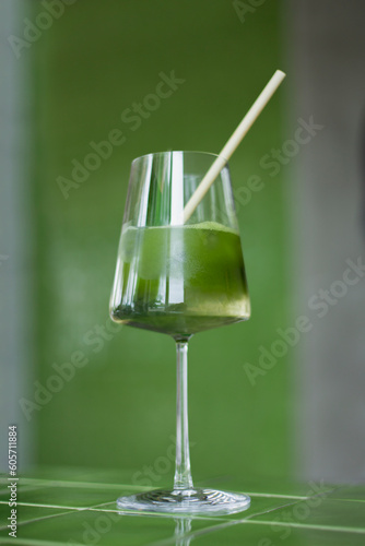 Making Japanese iced matcha latte, green tea with milk, soy milk, traditional matcha tools, with bamboo straw in glass on green background. Cocktail in wineglass.