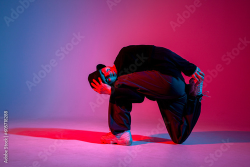 guy hiphop performer break dance in neon club lighting and doing acrobatic trick, male dancer stands in acrobatic pose