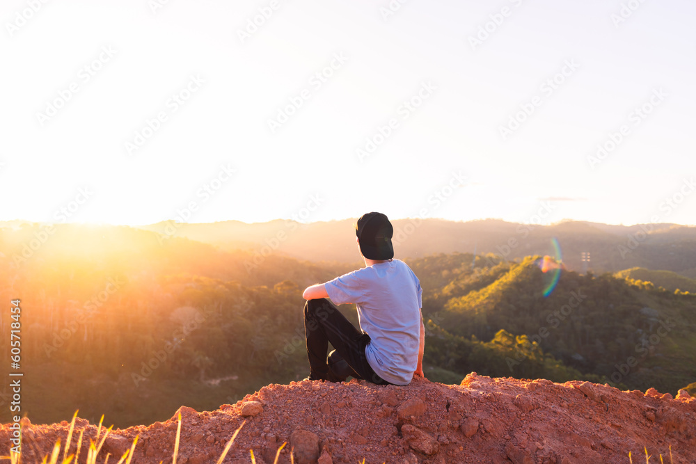 Man sitting on top of a mountain while contemplating the sunset. Person having reflections and thoughts while contemplating the landscape.