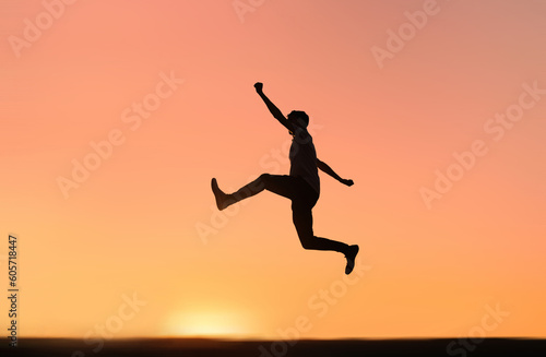 Silhouette of a happy man jumping to success and happiness with the orange sunset sky in the background.