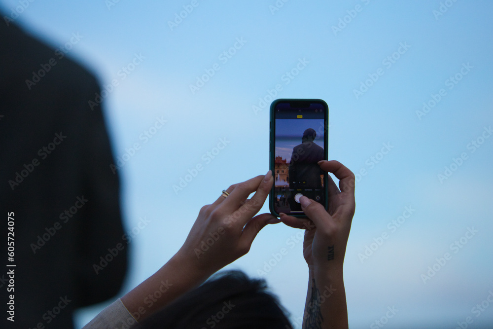 Woman taking a photo with her mobile phone of a statue in the most famous square of seville in spain. in the mobile phone you can see the monument and the statue from behind.