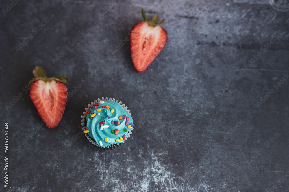 On a textured dark background, cakes and strawberries.