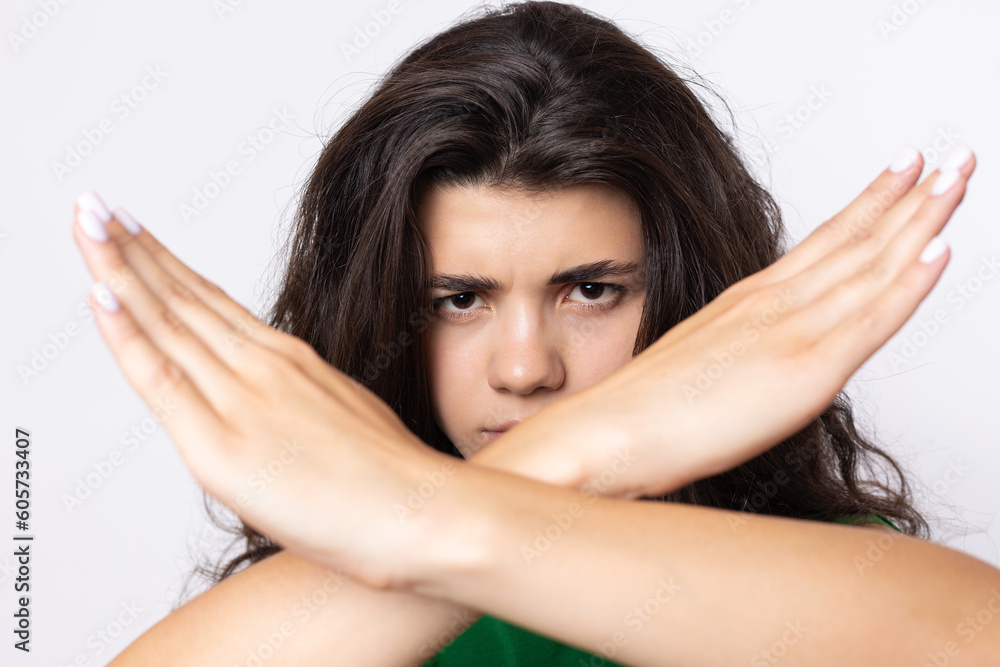 Fototapeta premium Portrait of a serious young woman showing stop gesture with her palm over white background