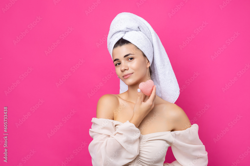 Beautiful cheerful attractive girl with a towel on her head, holds a sponge in the form of a pink heart. Beautiful cheerful attractive girl with a towel on her head, holds a sponge in the form of a pink heart.