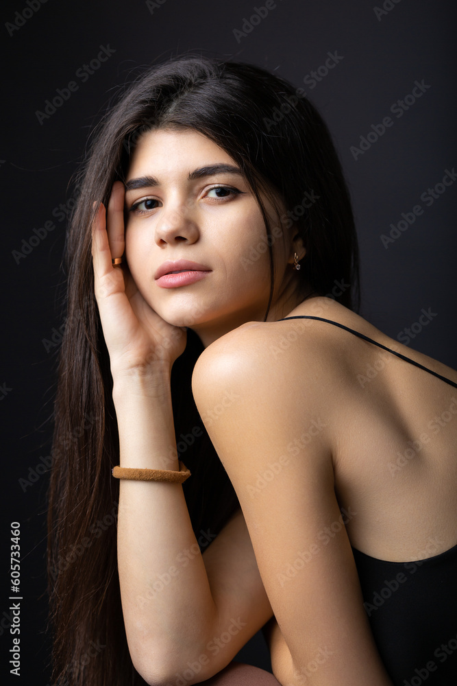 Classic studio portrait of a young brunette dressed in a black top, who is sitting on a chair against a black background. Classic studio portrait of a young brunette dressed in a black top, who is sitting on a chair against a black background.