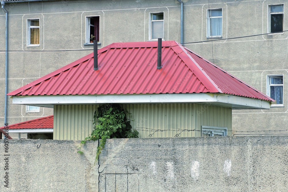 Naklejka premium red tiled metal roof on a small private house behind a gray concrete fence wall on the street