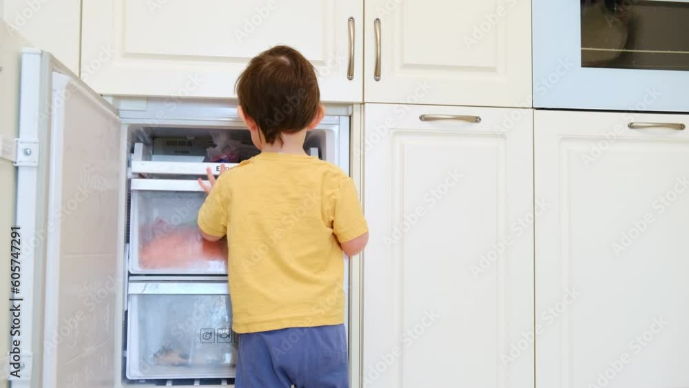 The child is playing near the open door of the freezer. The baby is looking at the white fridge, wondering what's inside. Kid aged about two years (one year ten months) The child is playing near the open door of the freezer. The baby is looking at the white fridge, wondering what's inside. Kid aged about two years (one year ten months)