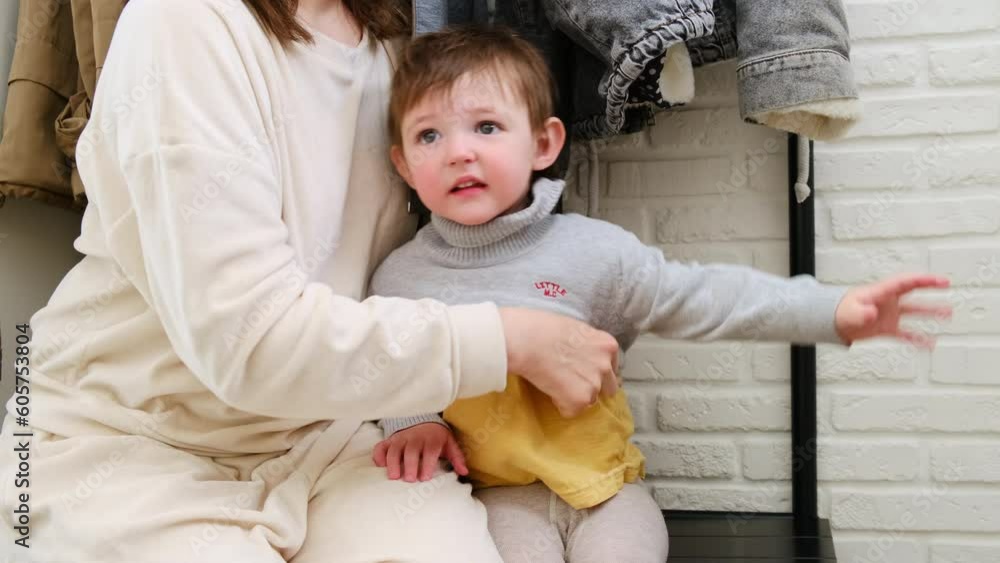 The woman picks out a warm sweater for her baby boy to wear on their tripю A happy parent changes their child into a clothes to stay cozy during their outdoor walk. Kid aged about two years The woman picks out a warm sweater for her baby boy to wear on their tripю A happy parent changes their child into a clothes to stay cozy during their outdoor walk. Kid aged about two years