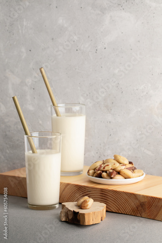 Two glasses with vegan plant based milk made of brazil nuts, plate of nuts on wooden board on gray.