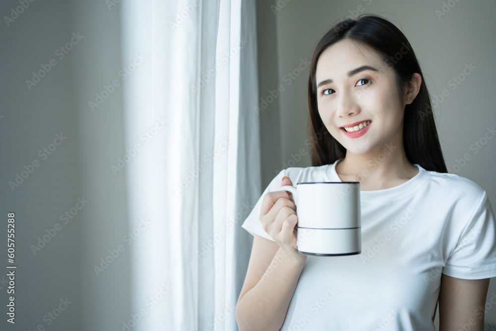 Asian women drinking coffee and wake up in her bed fully rested and open the curtains in the morning to get fresh air on sunshine Asian women drinking coffee and wake up in her bed fully rested and open the curtains in the morning to get fresh air on sunshine