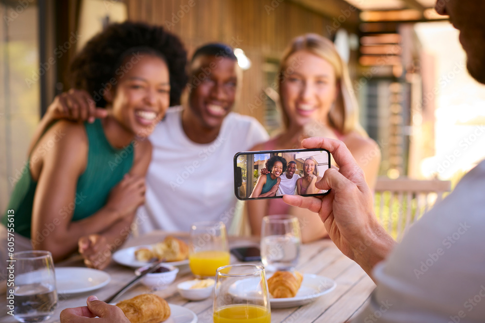 Group Of Multi-Cultural Friends Posing For Selfie On Mobile Phone Eating Breakfast Outdoors At Home