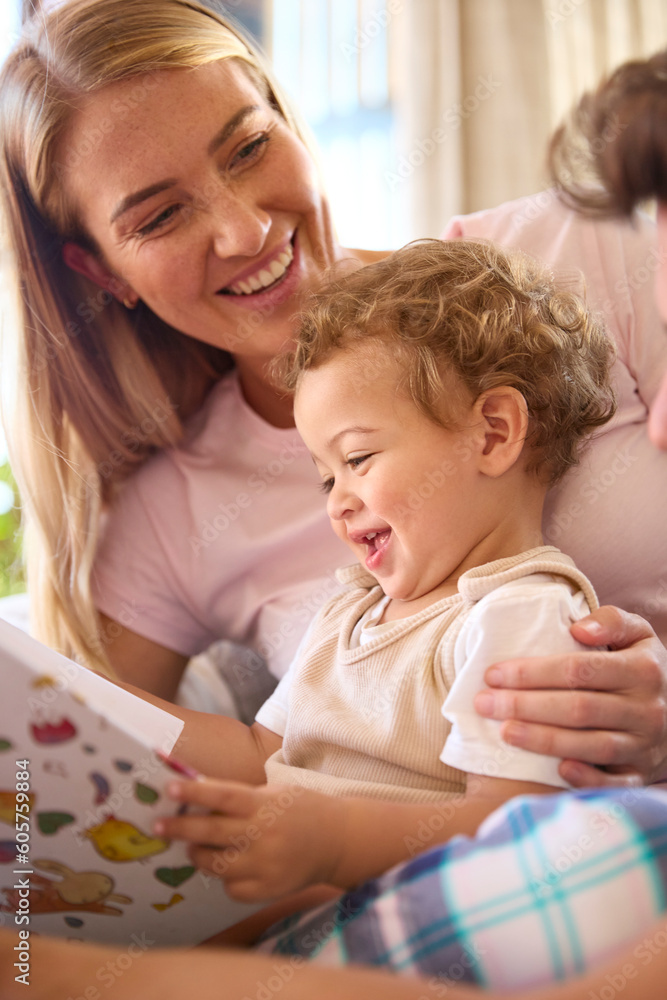 Family Sitting On Sofa At Home With Parents Reading Book With Young Son Family Sitting On Sofa At Home With Parents Reading Book With Young Son