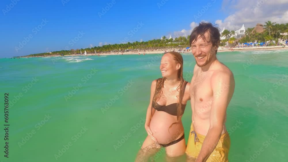 A slow-motion stock video captures a pregnant woman and a man joyfully exploring the tropical sea. They walk hand in hand, capturing their holiday memories with a selfie video using an action camera. A slow-motion stock video captures a pregnant woman and a man joyfully exploring the tropical sea. They walk hand in hand, capturing their holiday memories with a selfie video using an action camera.