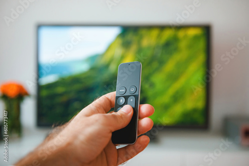 A young adult lies comfortably in their home, holding a remote control and turning on the television set. They focus on modern technology as they enjoy the cozy domestic life of watching TV indoors