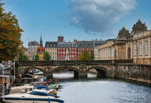 Copenhagen, Denmark - September 14, 2010: Marmorbroen, historic bridge over canal leading to Christiansborg Slot under blue cloudscape. Colored facades in back, small boats and green foliage