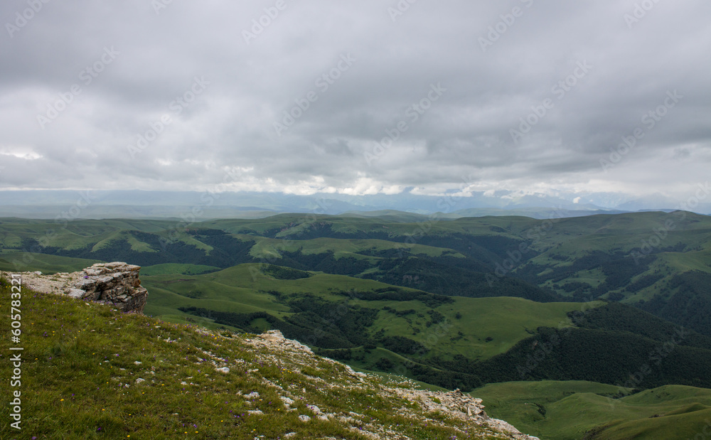 Fantastic dramatic landscape - panoramic view of the hilly valley blurred in the morning fog from the Bermamyt plateau in Karachay-Cherkessia on a cloudy summer day