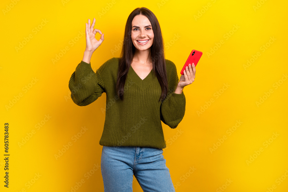 Photo of confident cool woman dressed khaki sweater showing okey gesture chatting modern device isolated yellow color background Photo of confident cool woman dressed khaki sweater showing okey gesture chatting modern device isolated yellow color background