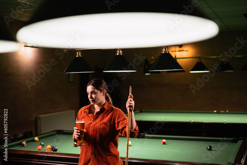 Caucasian beautiful woman drinking beer near billiard table in billiard club