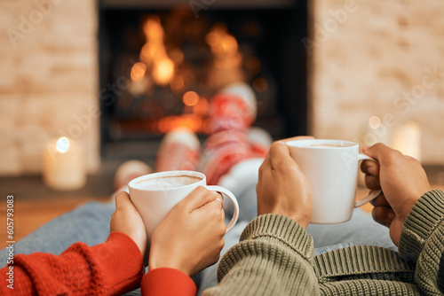 Hands, coffee and couple relax by fireplace, bonding and cozy in home together. Tea, man and woman relaxing by fire on Christmas holiday in winter, heat and enjoying quality time with drinks in house photo