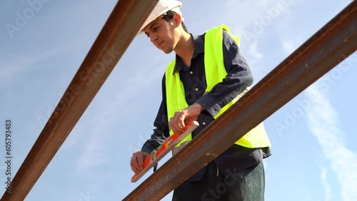 Young Arab worker checking the angulation of the beams of the roof of a house with a spirit level. Wearing high visibility vest and white helmet. Concept of construction professionals. photo