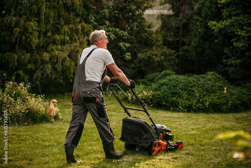 Fotografia The male worker mows the grass on the site, cares for the garden, uses a gasolin