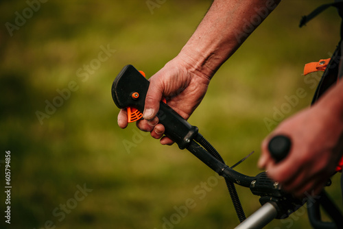 Male hands turning on the grass trimmer. Focus on a machine,