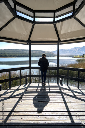 Elderly woman standing against the light under a pergola contemplates the landscape of the Zeta lagoon in Esquel, Chubut, Argentine Patagonia. photo