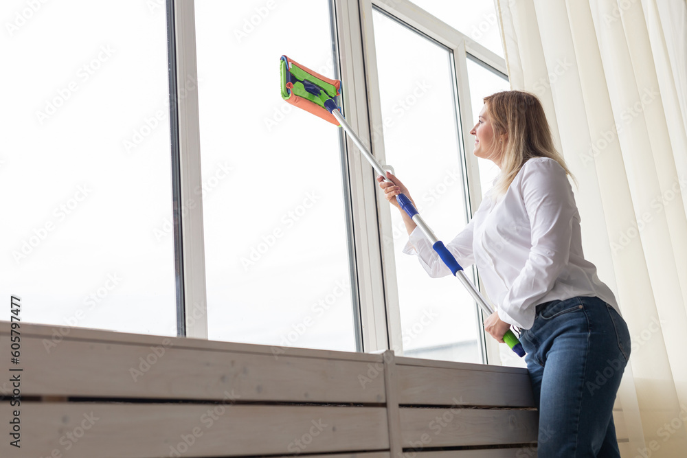 Happy woman cleaning window with sponge mop at home - housework and housekeeping concept