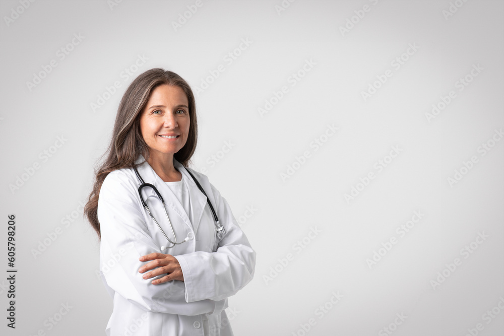 Portrait of cheerful senior european woman doctor in white coat with stethoscope standing with folded arms, copy space Portrait of cheerful senior european woman doctor in white coat with stethoscope standing with folded arms, copy space