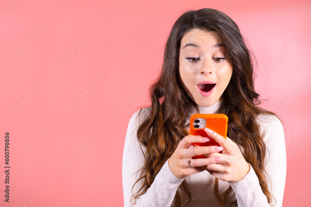 Portrait of an excited young woman surprised looking at the cellphone isolated over pink background. Portrait of an excited young woman surprised looking at the cellphone isolated over pink background.