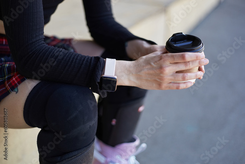 Skater girl sitting in a skatepark with a cup of coffee. Unrecognizable female person wearing inline skates and protective knee pads