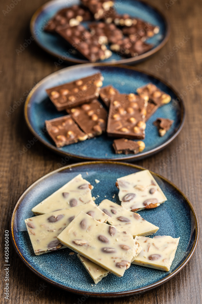 Broken chocolate bars with nuts on wooden table. Broken chocolate bars with nuts on wooden table.